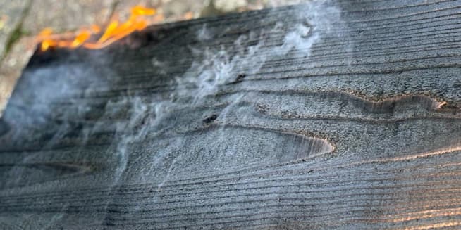 Smoke rising from freshly charred Yakisugi cedar board showing detailed wood grain and cooling surfac