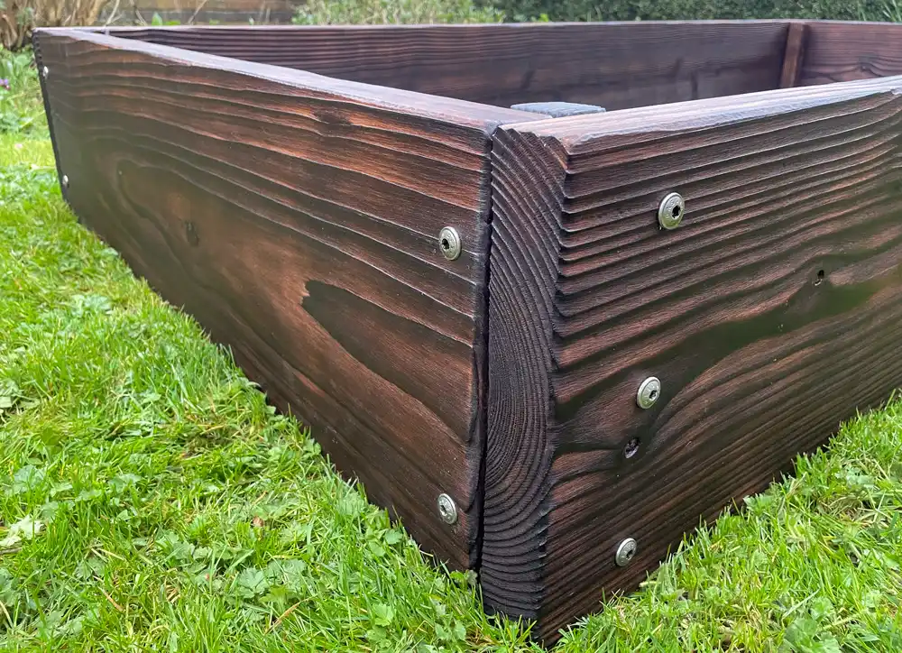 Thick timber raised bed corner showing structural fixings designed to reduce bowing risk
